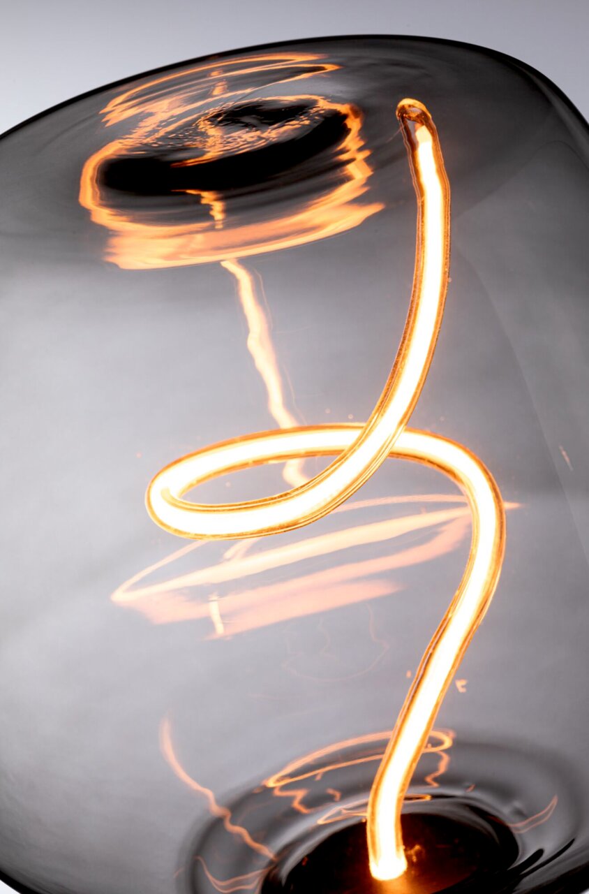 Nahaufnahme einer leuchtenden LED-Glühbirne mit geschwungenem Filament, seitliche Perspektive