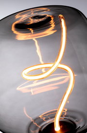 Nahaufnahme einer leuchtenden LED-Glühbirne mit geschwungenem Filament, seitliche Perspektive