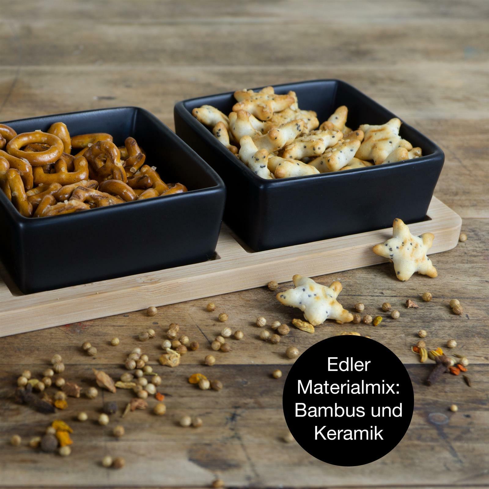 Servierset aus Bambus mit drei schwarzen Keramikschalen, gefüllt mit Snacks, auf einem Holztisch aus der Vogelperspektive