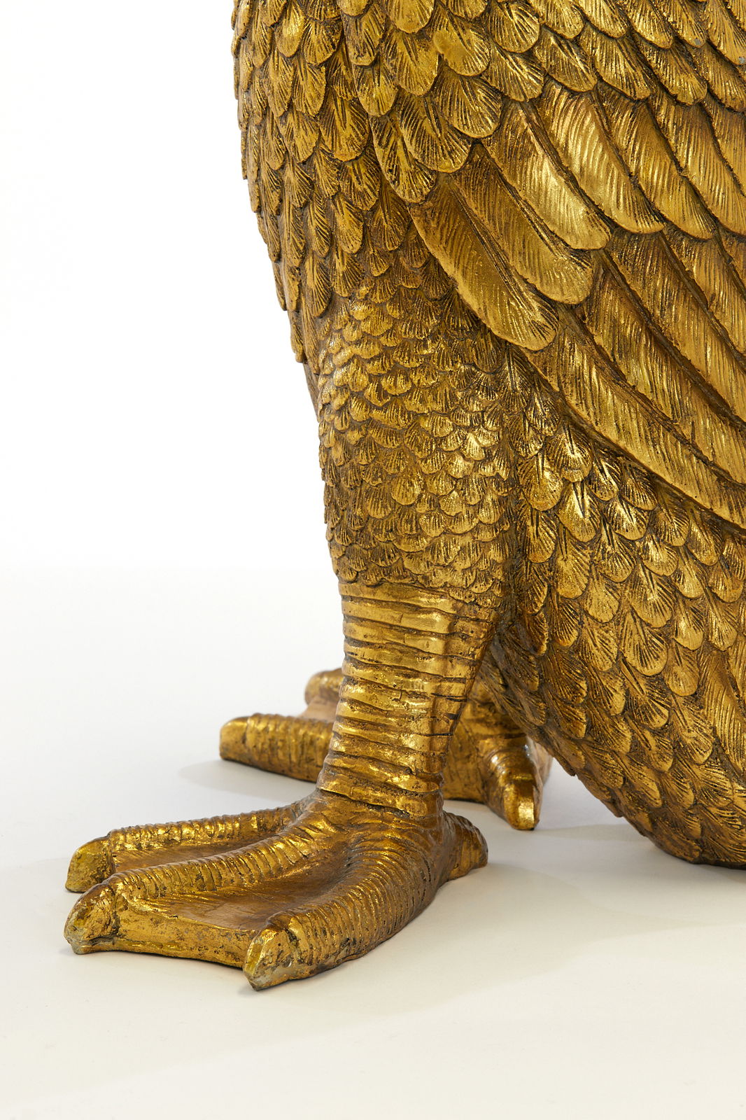 Nahaufnahme eines goldenen Tischleuchtenfußes in Form eines Vogelfußes mit detaillierten Federn, seitliche Perspektive.