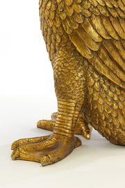 Nahaufnahme eines goldenen Tischleuchtenfußes in Form eines Vogelfußes mit detaillierten Federn, seitliche Perspektive.