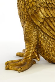 Nahaufnahme eines goldenen Tischleuchtenfußes in Form eines Vogelfußes mit detaillierten Federn, seitliche Perspektive.