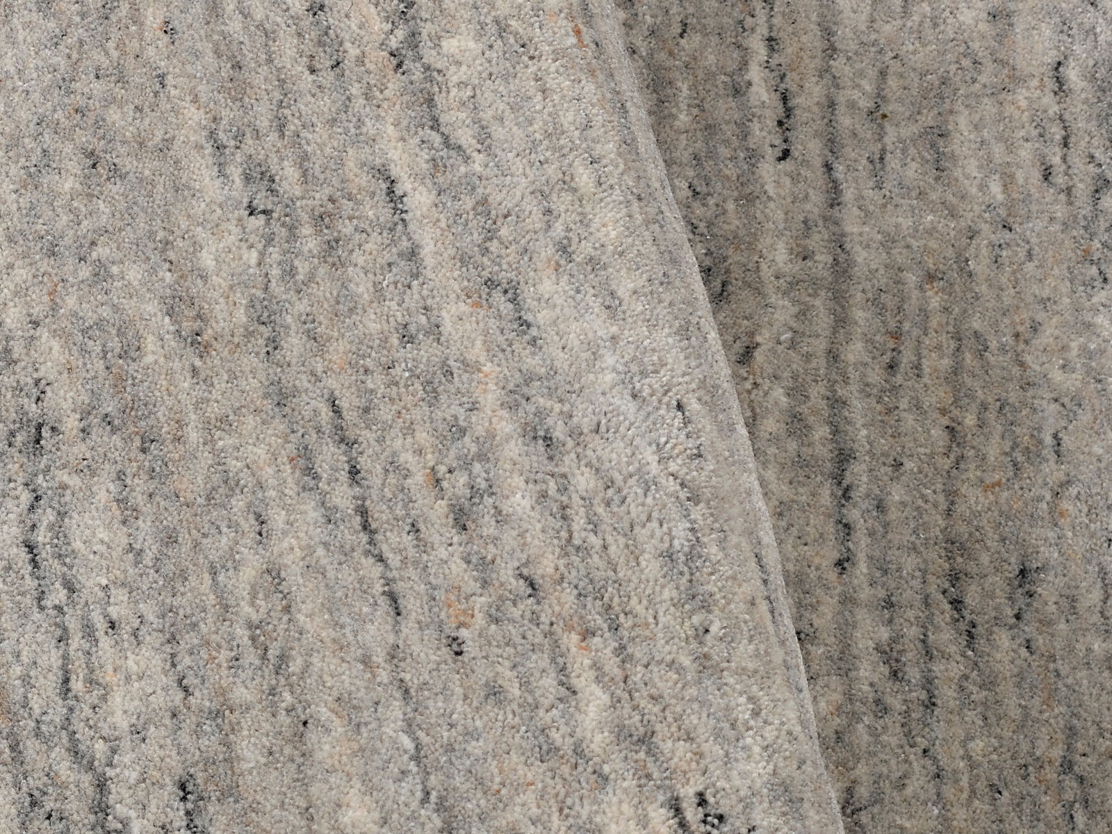 Nahaufnahme eines grauen Wollteppichs mit feiner Textur und subtilen Farbvariationen, von oben betrachtet.