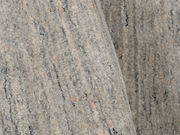 Nahaufnahme eines grauen Wollteppichs mit feiner Textur und subtilen Farbvariationen, von oben betrachtet.