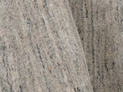 Nahaufnahme eines grauen Wollteppichs mit feiner Textur und subtilen Farbvariationen, von oben betrachtet.