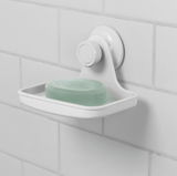 Weiße Seifenschale mit Gel-Lock-Technologie, an einer gefliesten Wand befestigt, mit einem Stück grüner Seife. Seitenansicht.