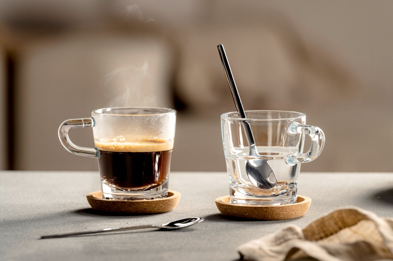 Twee glazen espressokopjes met schoteltjes, één met espresso en één met water, gefotografeerd vanuit een zijaanzicht.
