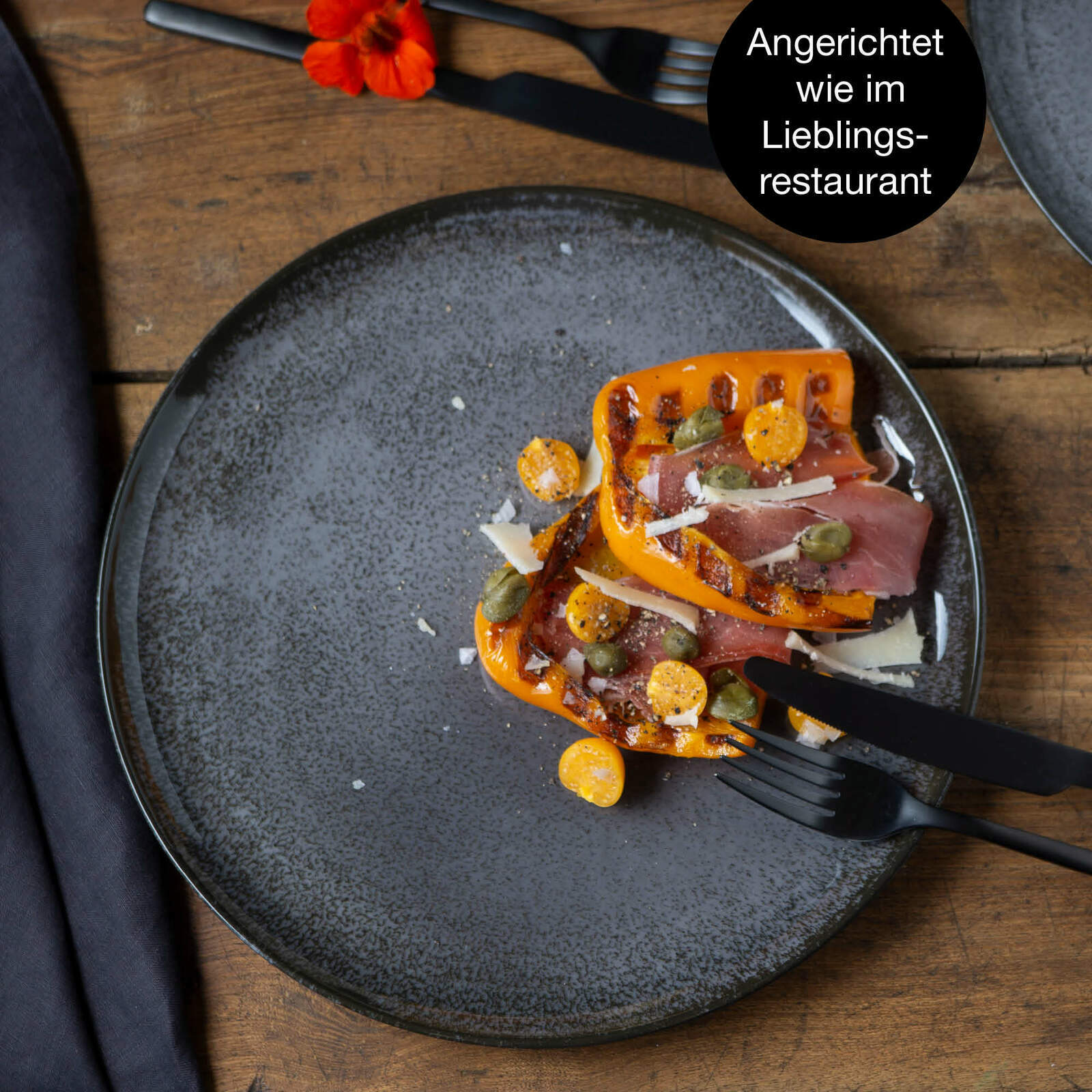 Anthrazitfarbener Teller mit gegrilltem Gemüse und Schinken, aus der Vogelperspektive fotografiert.