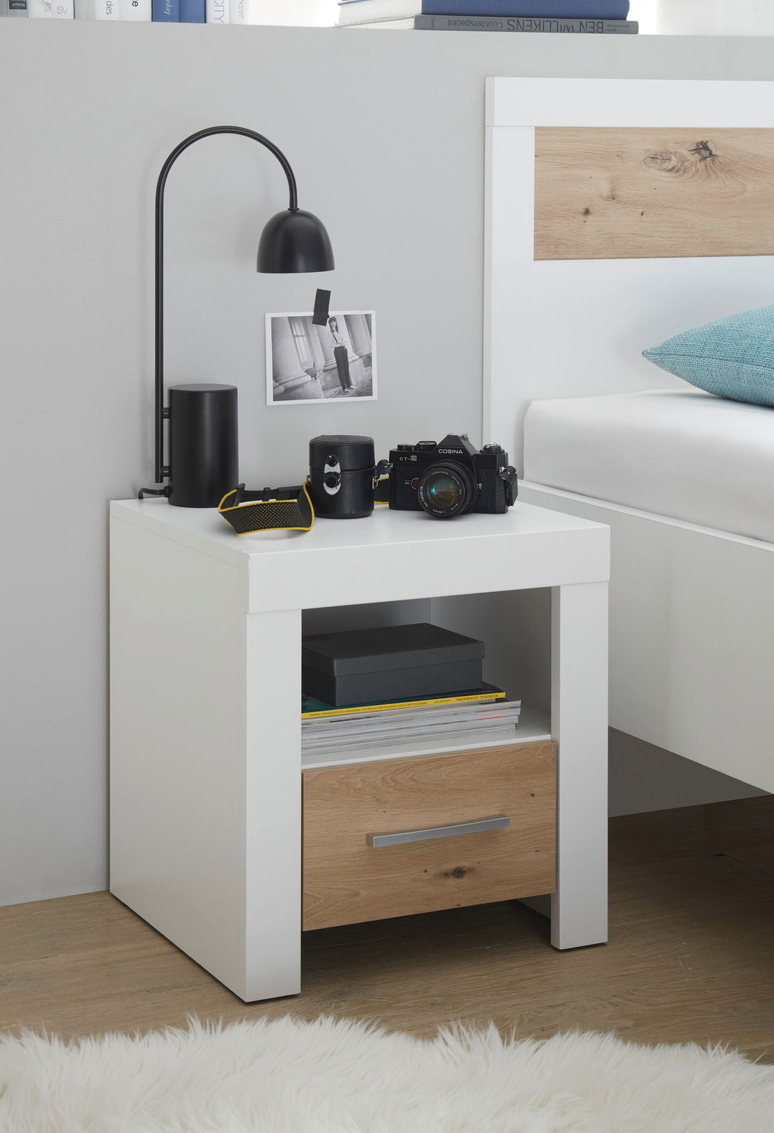 Moderne Nachtkommode in Weiß mit Holzschublade, dekoriert mit Lampe und Kamera, seitliche Perspektive