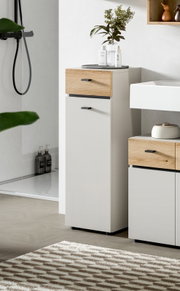 Moderner Bad-Hochschrank in Weiß mit Eichenholz-Schubladenfront und schwarzen Griffen, seitliche Perspektive im Badezimmer neben Waschbecken und Dusche