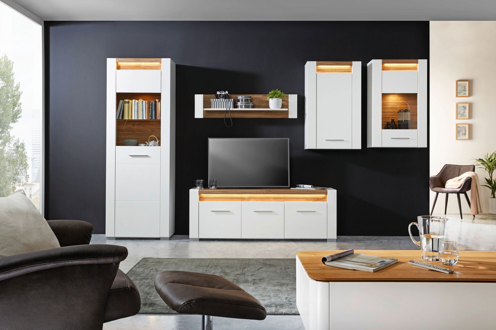 Moderne Wohnzimmermöbel in Weiß mit Holzakzenten, bestehend aus Vitrinen, TV-Unterteil und Wandboard, frontal betrachtet.