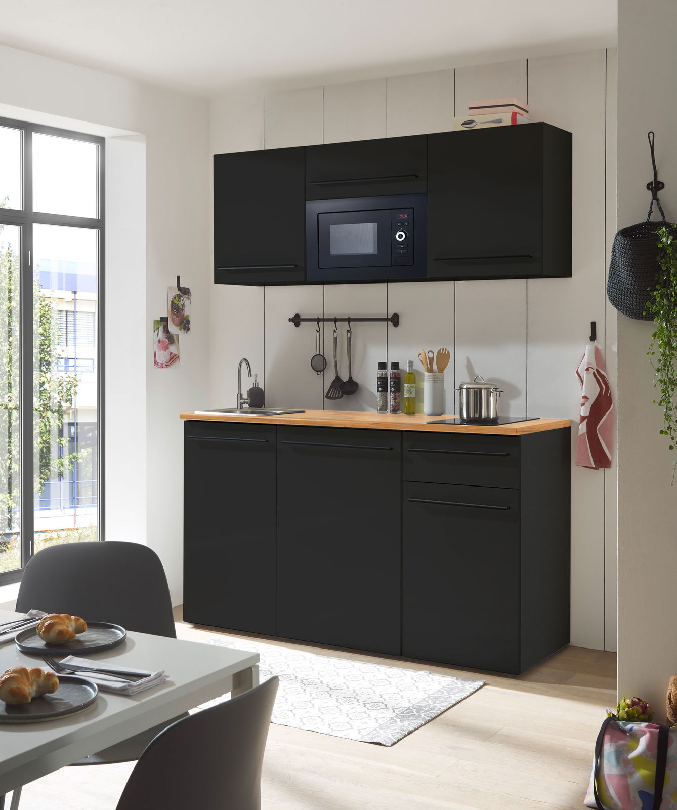 Moderne Single-Küche in schwarzem Design mit eingebauter Mikrowelle, Spüle und Arbeitsfläche aus Holz, frontal betrachtet.