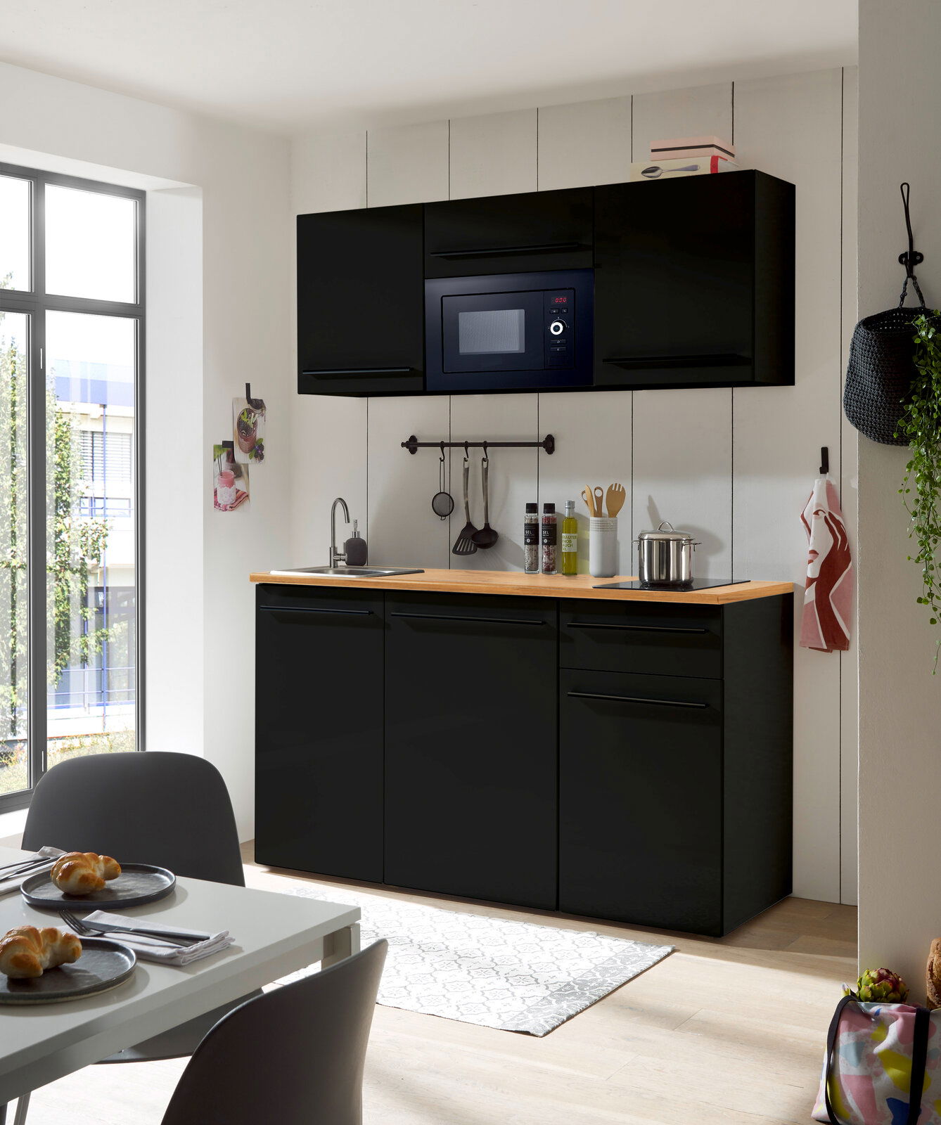 Moderne Single-Küche in schwarzem Design mit eingebauter Mikrowelle, Spüle und Arbeitsfläche aus Holz, frontal betrachtet.