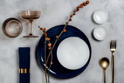 Een elegante set met champagneglazen en dessertschaaltjes, gezien van bovenaf in een stijlvolle tafeldecoratie, met goudkleurig bestek en blauwe accenten.
