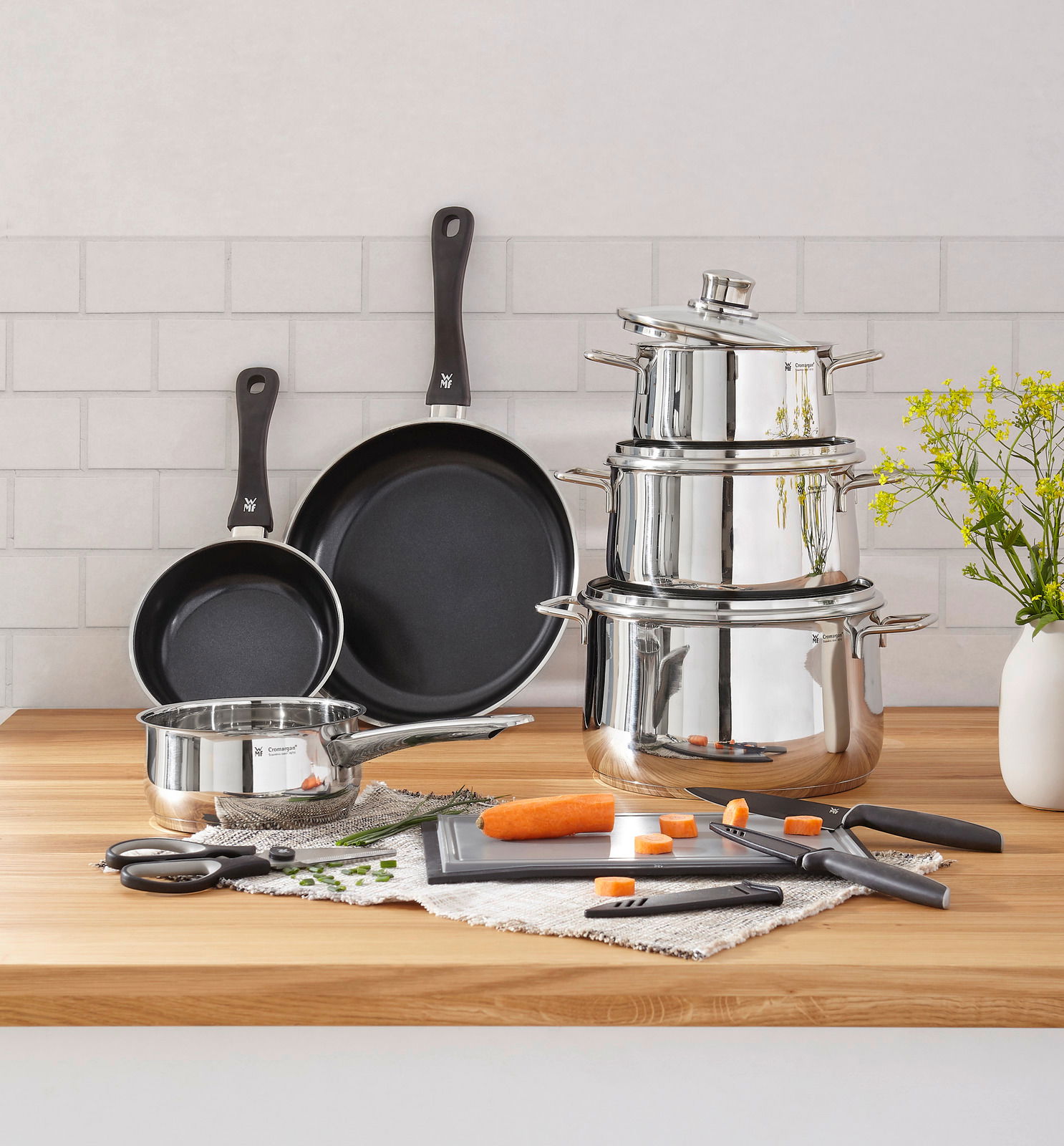 Kochtopf-Starter-Set 10-tlg. aus Edelstahl mit Töpfen, Pfannen und Küchenutensilien auf einer Holzarbeitsplatte, seitliche Perspektive.