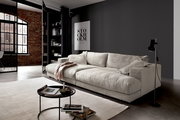 Modernes, cremefarbenes Megasofa in einem stilvollen Wohnzimmer mit Ziegelwand und großen Fenstern, seitliche Perspektive.
