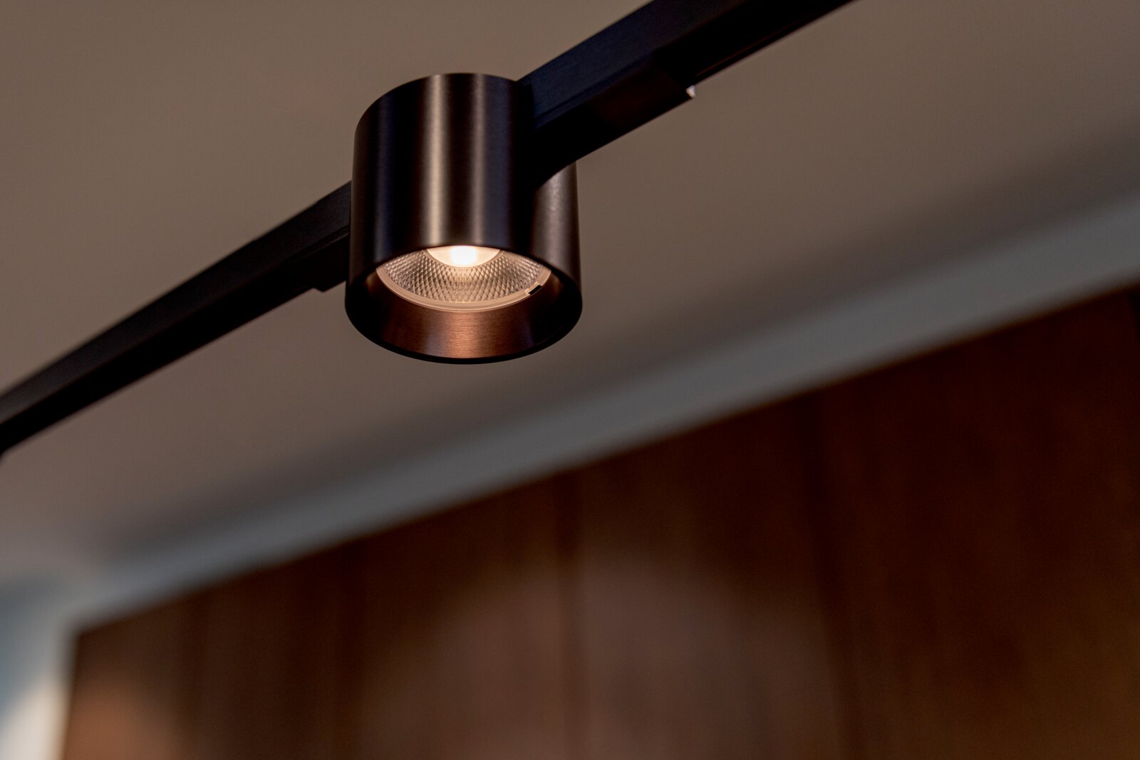 Zwarte cilindervormige LED-spot op een rail, warm wit licht, gefotografeerd van onderaf in een moderne interieursetting