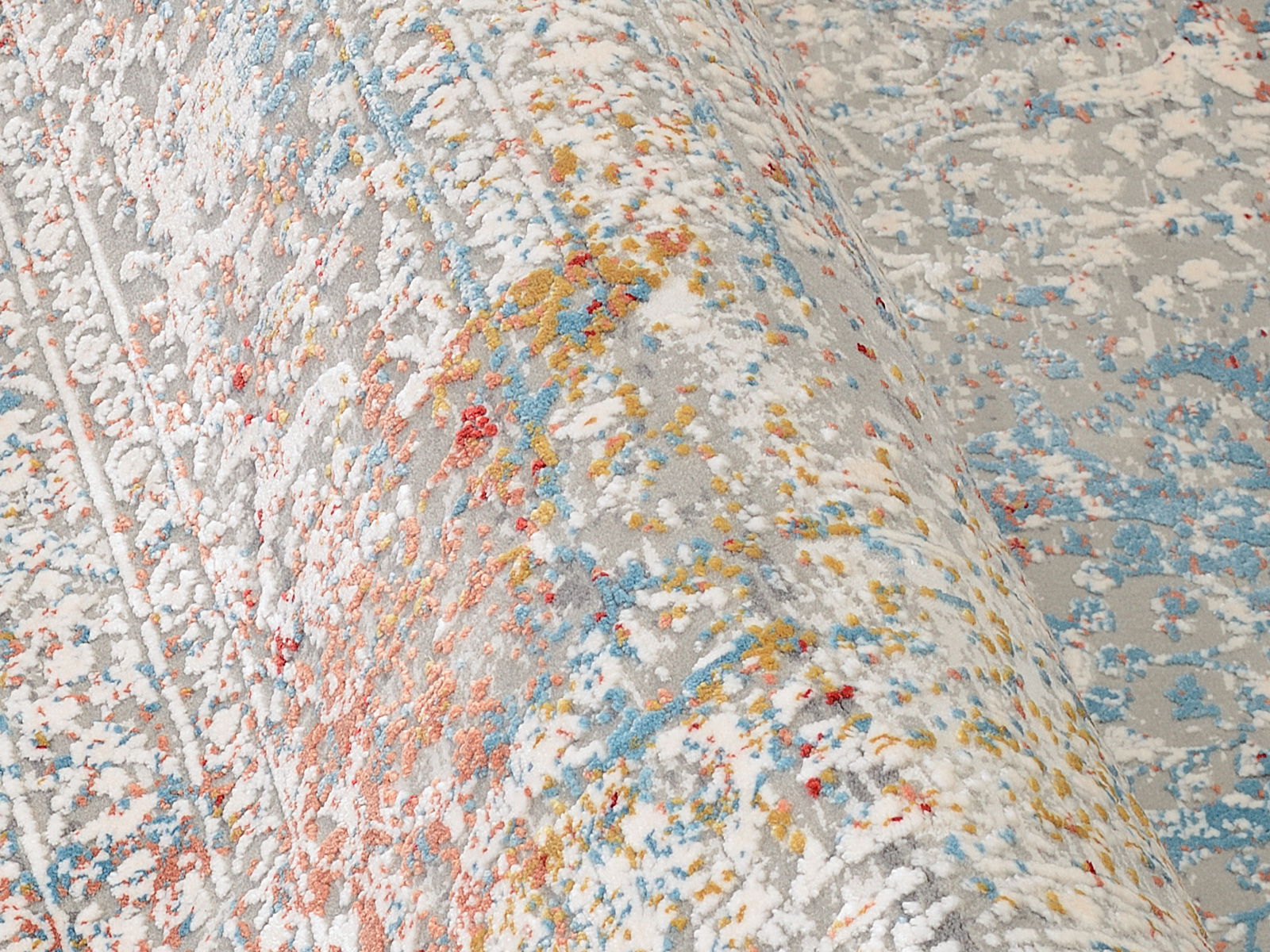 Nahaufnahme eines Designer-Teppichs mit abstraktem Muster in Grau, Blau, Rot und Gelb, perspektivisch von der Seite aufgenommen.