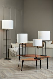 Vier moderne Lampen mit weißen zylindrischen Lampenschirmen und schwarzen Ständern, in einem stilvollen Raum mit Holzboden und neutralen Wänden, aus einer seitlichen Perspektive fotografiert.