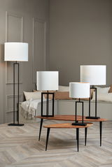 Vier moderne Lampen mit weißen zylindrischen Lampenschirmen und schwarzen Ständern, in einem stilvollen Raum mit Holzboden und neutralen Wänden, aus einer seitlichen Perspektive fotografiert.