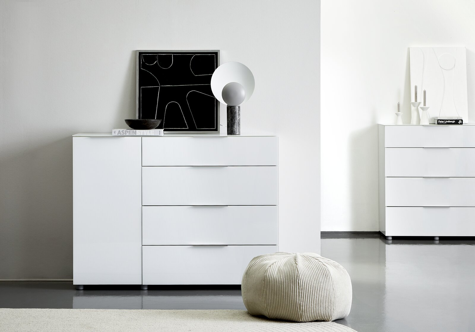 Weiße Kombikommode mit vier Schubladen und einer Tür, dekoriert mit einem modernen Kunstwerk und einer Lampe, aus der Frontalperspektive fotografiert.