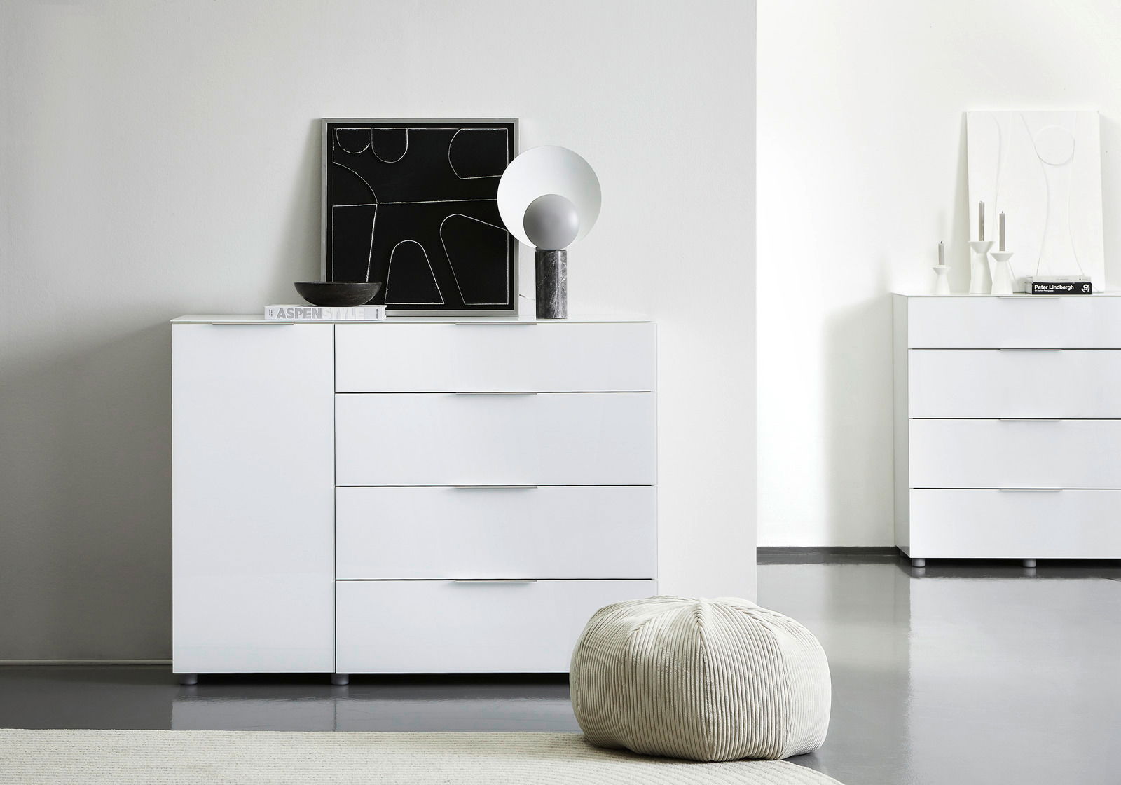 Weiße Kombikommode mit vier Schubladen und einer Tür, dekoriert mit einem modernen Kunstwerk und einer Lampe, aus der Frontalperspektive fotografiert.