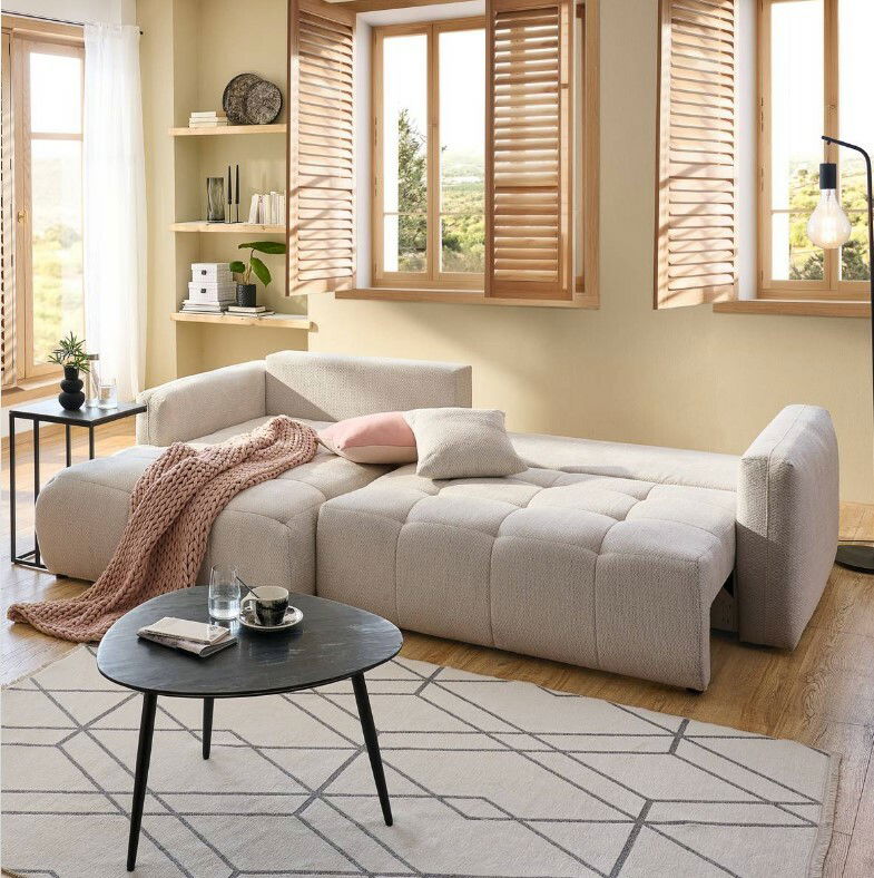 Ecksofa London in einem modernen Wohnzimmer, beige gepolstert, mit Kissen und Decke, aus der Perspektive von vorne links.