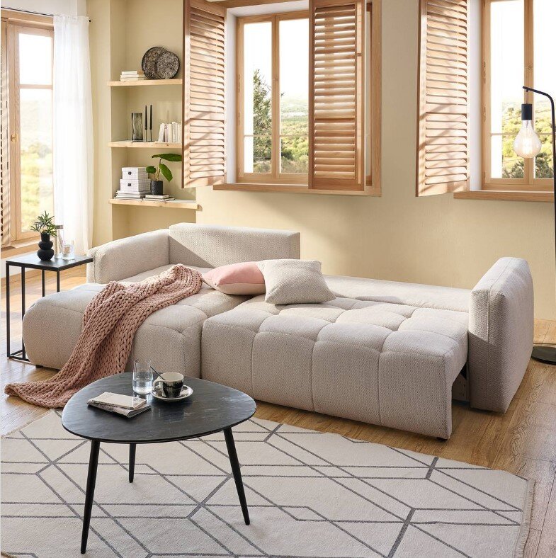 Hoekbank London in een moderne woonkamer, beige gestoffeerd, met kussens en een deken, gezien vanaf links vooraan.