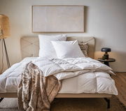 Gemütliches Schlafzimmer mit einer Daunendecke in der Größe 155x220 cm auf einem Bett, umgeben von Kissen und einer stilvollen Lampe, aus der Perspektive von vorne betrachtet.