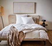 Gemütliches Schlafzimmer mit einer Daunendecke in der Größe 155x220 cm auf einem Bett, umgeben von Kissen und einer stilvollen Lampe, aus der Perspektive von vorne betrachtet.