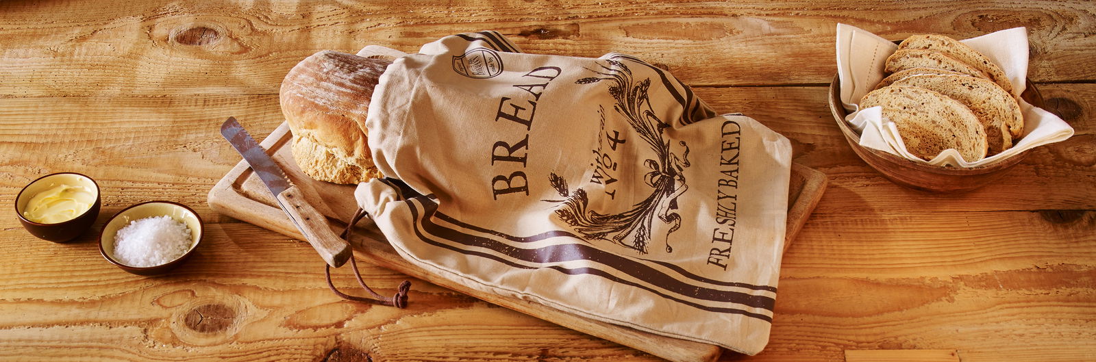 Brotbeutel mit der Aufschrift 'Freshly Baked' auf einem Holztisch, gefüllt mit einem Laib Brot. Perspektive von oben.
