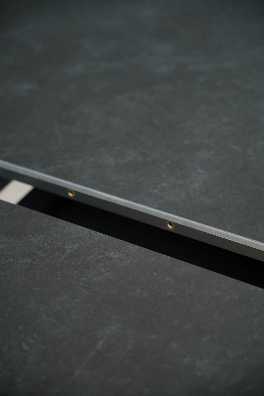 Nahaufnahme eines Esstisches mit dunkler, strukturierter Oberfläche und Metallkante, seitliche Perspektive