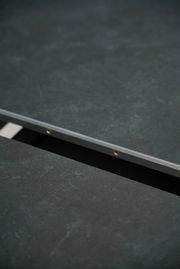 Nahaufnahme eines Esstisches mit dunkler, strukturierter Oberfläche und Metallkante, seitliche Perspektive