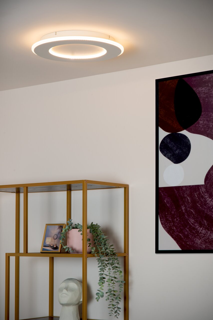Moderne plafondlamp Lucide AXELLE in ronde vorm, gezien van onderaf, met een warme lichtschijn op het plafond van een stijlvol ingerichte ruimte.