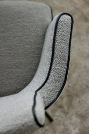 Close-up van een lichtgrijze bouclé-stoel met zwarte bies aan de armleuning, zijaanzicht schuin van bovenaf