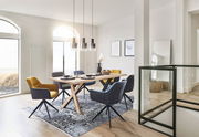 Moderner Esstisch mit Holztischplatte und X-förmigen Beinen, umgeben von stilvollen Stühlen in einem hellen, eleganten Esszimmer. Perspektive von der Seite.
