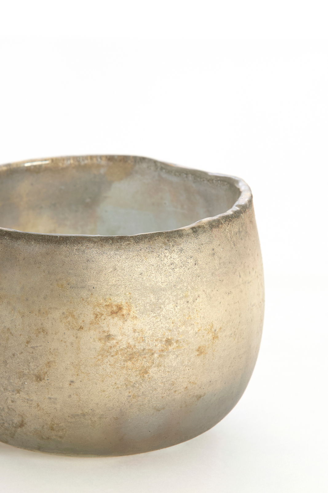 Nahaufnahme eines rustikalen, goldfarbenen Teelichthalters mit unregelmäßiger Oberfläche und leicht ungleichmäßigem Rand.