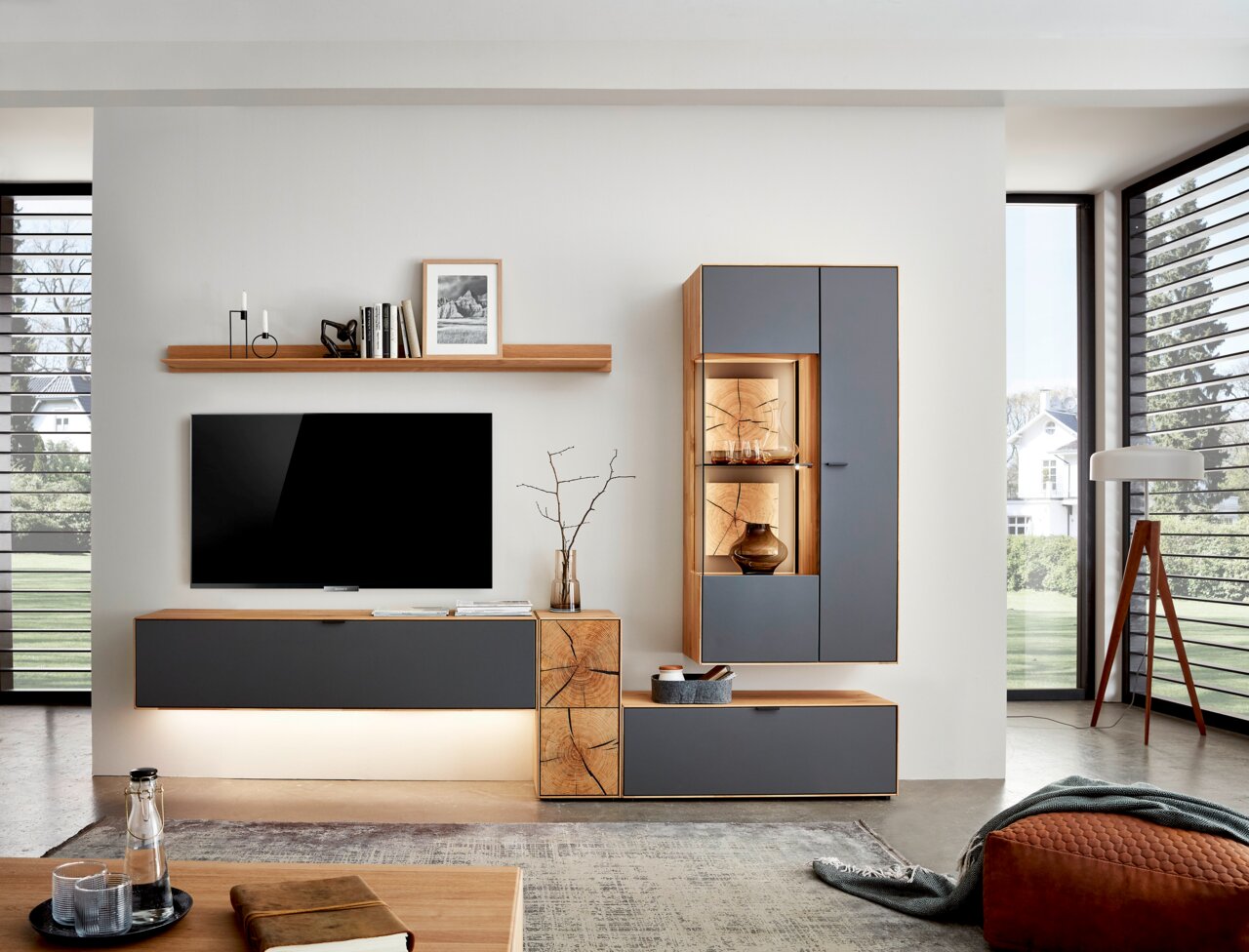 Moderne wandcombinatie in een woonkamer met grijze en houtkleurige elementen, bestaande uit een tv-kast, een hangkast met vitrine en een boekenplank. Perspectief: vooraanzicht.