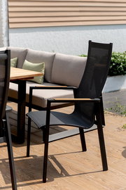 Moderner schwarzer Stapelsessel mit hoher Rückenlehne und Armlehnen aus Holz, seitliche Perspektive auf einer Terrasse neben einem Holztisch und einem Sofa.