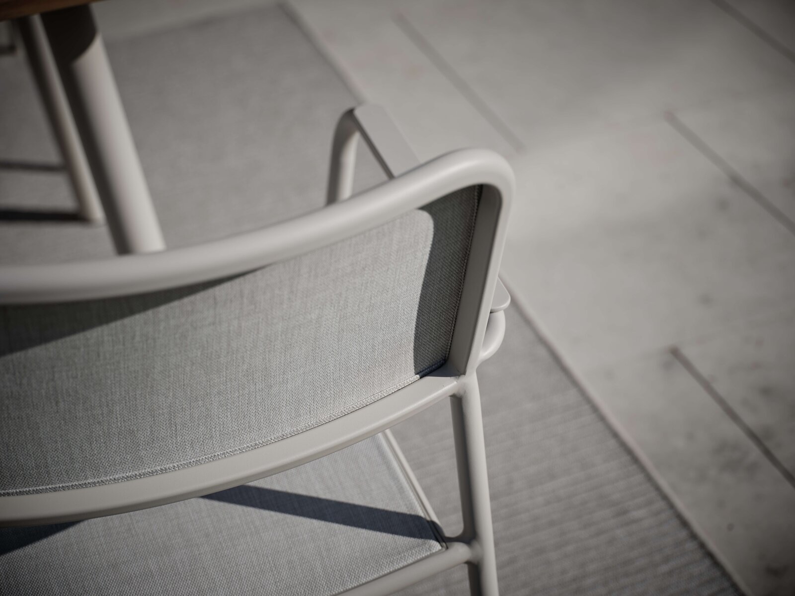 Rückansicht eines modernen Stapelsessels mit grauem Stoffbezug und hellem Metallrahmen auf einer Terrasse.