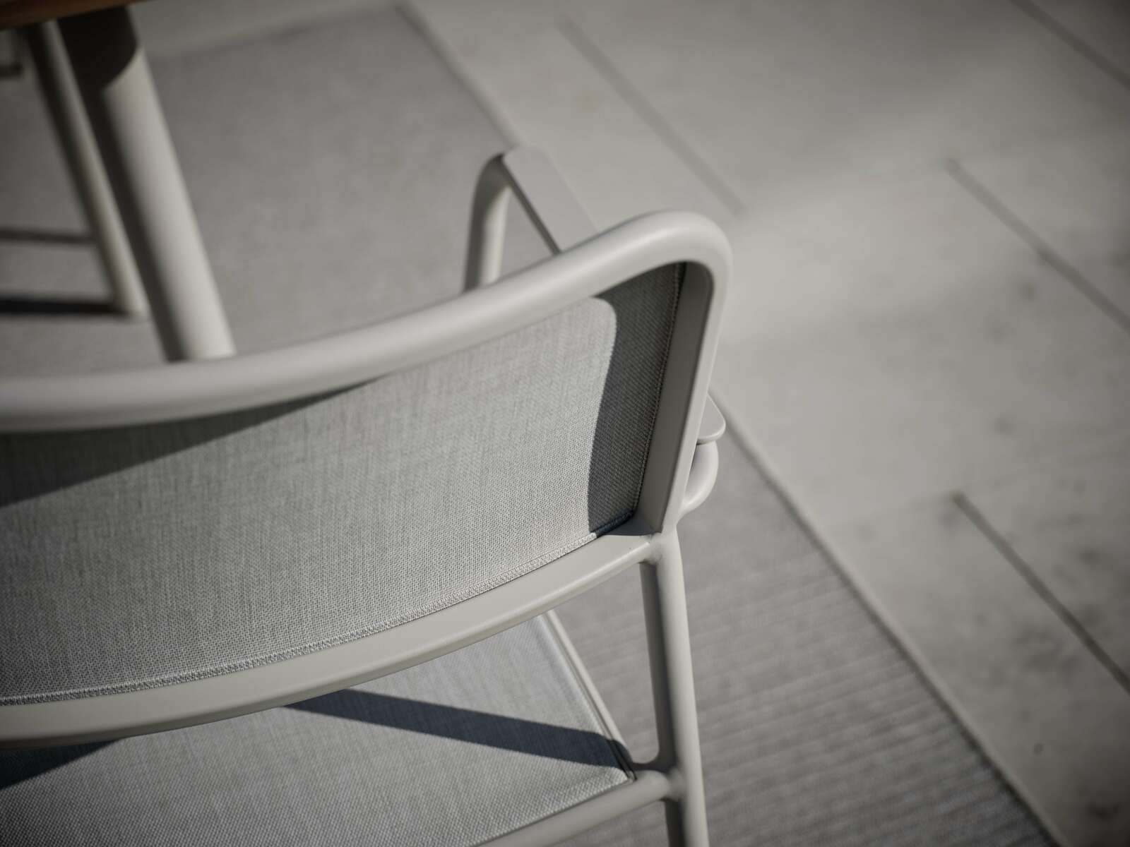 Rückansicht eines modernen Stapelsessels mit grauem Stoffbezug und hellem Metallrahmen auf einer Terrasse.