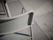 Rückansicht eines modernen Stapelsessels mit grauem Stoffbezug und hellem Metallrahmen auf einer Terrasse.