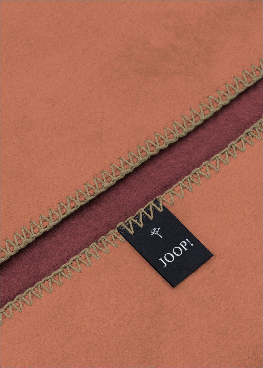 Nahaufnahme einer zweifarbigen Decke mit Zierstich und Joop-Label, Perspektive von oben.