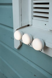 Drie witte, ronde wandhaken in de vorm van een ei aan een wit raamkozijn, close-up vanuit zijdelingse hoek.