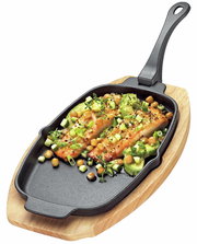 Servierpfanne mit abnehmbarem Griff, gefüllt mit gebratenem Lachs und Gemüse, auf einem Holzbrett, aus der Vogelperspektive