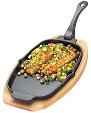 Servierpfanne mit abnehmbarem Griff, gefüllt mit gebratenem Lachs und Gemüse, auf einem Holzbrett, aus der Vogelperspektive