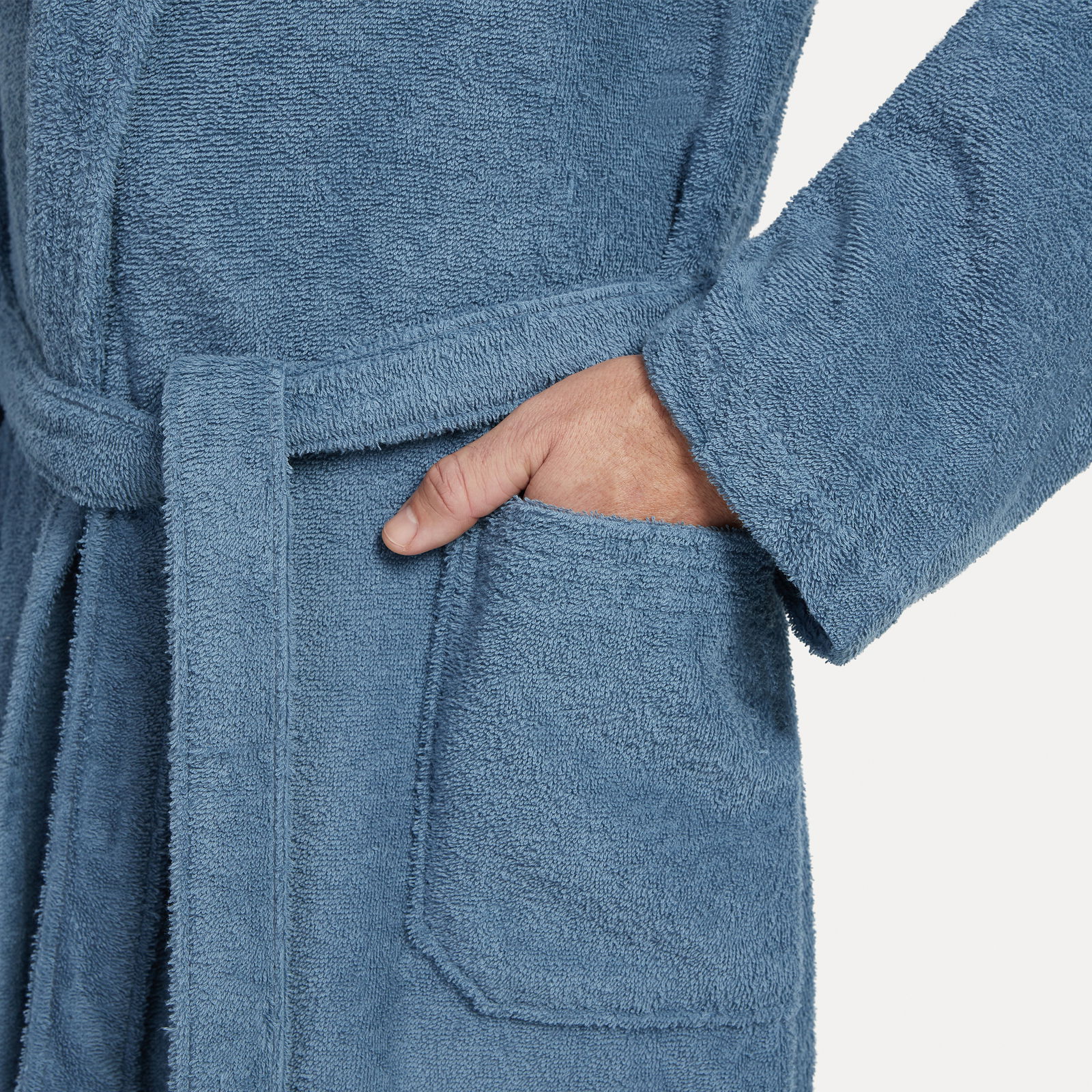 Nahaufnahme eines blauen Bademantels mit Schalkragen in Größe XL, zeigt eine Hand in der Tasche und den Gürtel.
