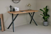 Moderner Schreibtisch mit Holzplatte und schwarzen Metallbeinen, seitliche Perspektive, dekoriert mit Lampe, Pflanzen und Schreibutensilien.
