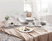 Ein stilvolles Kombiservice Rondo Weiß 30-tlg, präsentiert auf einem Tisch mit dekorativen Elementen und natürlichem Licht von einem Fenster im Hintergrund. Die Perspektive zeigt das Service von schräg oben.