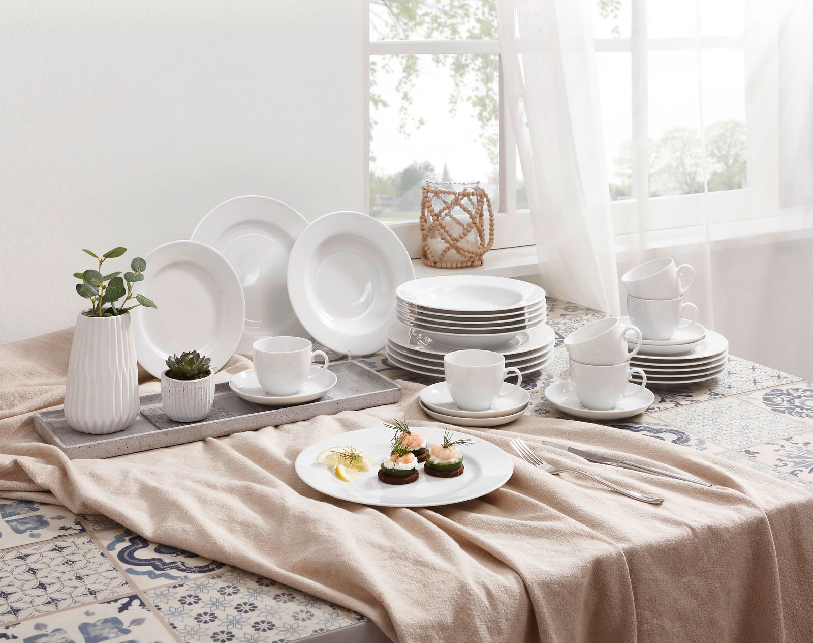 Seltmann Weiden Kombiservice 30-tlg. RONDO Ein stilvolles Kombiservice Rondo Weiß 30-tlg, präsentiert auf einem Tisch mit dekorativen Elementen und natürlichem Licht von einem Fenster im Hintergrund. Die Perspektive zeigt das Service von schräg oben.